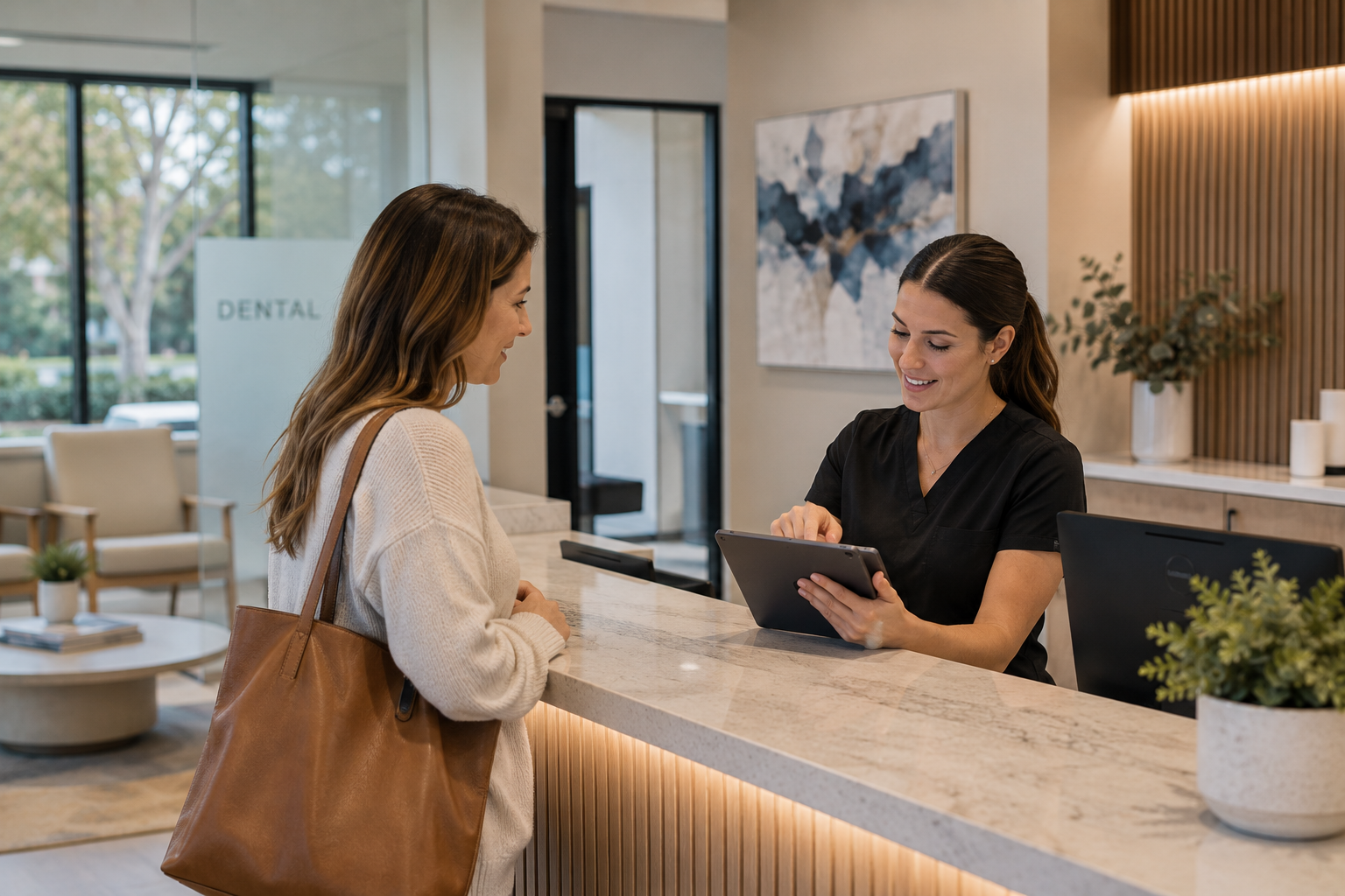 Front-desk professional assisting an adult patient with scheduling in a modern dental reception area.